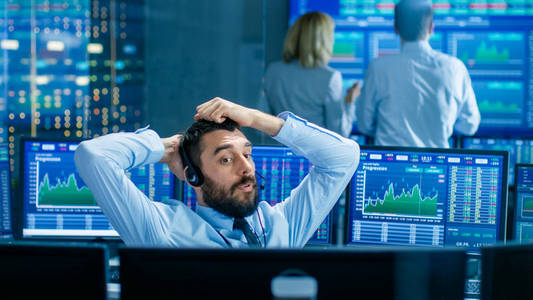 证券交易所交易员通过耳机与大客户达成交易。 他与其他经纪人合作，并被电脑包围，屏幕上有图表和滴答数字。