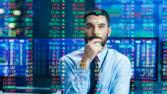 股票市场顶级交易者看预测的滴答数字和图表运行分析数据，以使最好的销售。 在他身后的房间里充满了屏幕和统计数据。