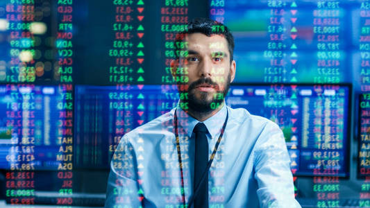 股票市场顶级交易者看预测的滴答数字和图表运行分析数据，以使最好的销售。 在他身后的房间里充满了屏幕和统计数据。