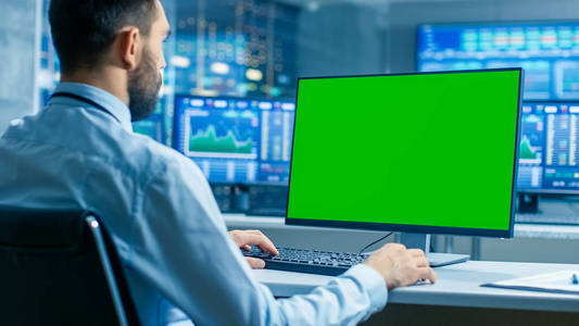 股票市场交易员在电脑上工作与孤立的模拟绿色屏幕。在背景监视器中显示股票勾号和图表。