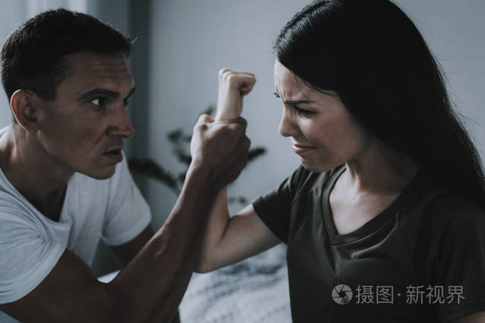 女人和男人在家里打架和争吵.已婚夫妇坐在灰色床上争吵的肖像.