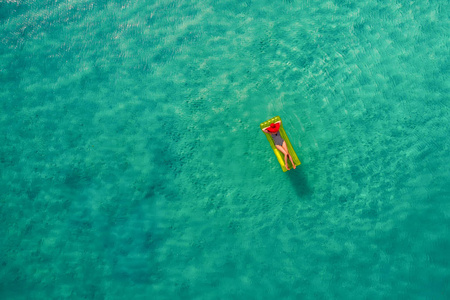 鸟瞰苗条的女人在塞舌尔透明的绿松石海的游泳床垫上游泳。 夏天海景与女孩美丽的波浪，五颜六色的水。 无人驾驶飞机的俯视图