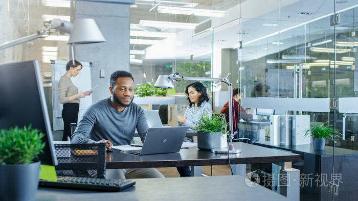 忙碌的国际办公室非裔美国人男子在他的办公桌上工作在后台女商人讨论