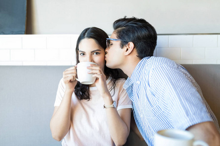 在咖啡馆喝咖啡时，可爱的年轻人亲吻对方的脸颊