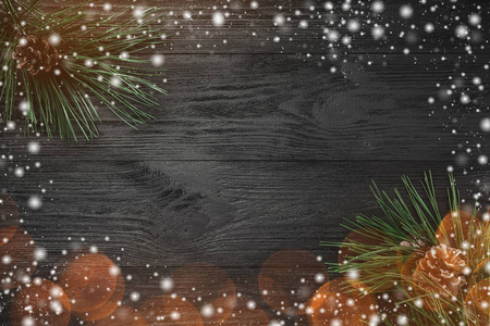 圣诞卡。 黑色木材背景与松树枝松果顶部视图。 圣诞贺卡有光和雪的效果。