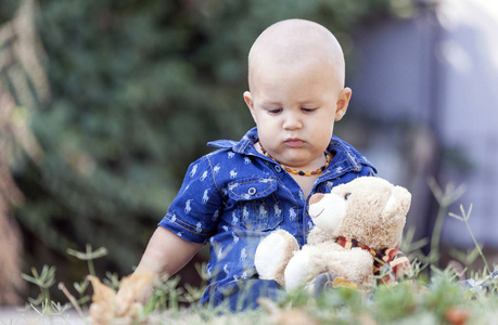 一个可爱的小男孩的肖像，坐在草地上，夏天玩他最喜欢的毛绒玩具