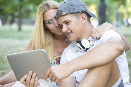 美丽快乐的年轻夫妇用平板电脑约会。 聊天在线拍摄美丽的公园在平板电脑拥抱。 女朋友和男朋友一起玩平板电脑