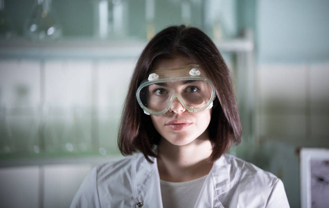化学实验室。在工作眼镜的年轻妇女看在相机
