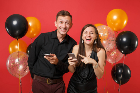 一对穿着黑色衣服的夫妇在手机上发短信庆祝生日，节日聚会被隔离在红色背景气球上。 圣瓦伦丁国际妇女节2019年新年快乐概念。 嘲弄