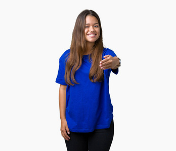 年轻漂亮的黑发女人穿着蓝色T恤，在孤立的背景上微笑，友好地提供握手作为问候和欢迎。 成功的生意。