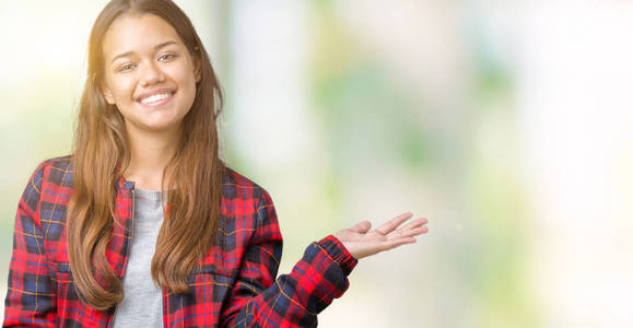 年轻漂亮的黑发女人穿着一件夹克，在孤立的背景上微笑，欢快的呈现，用手掌指着相机。