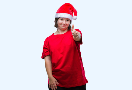 年轻的成年妇女患有唐氏综合症，戴着圣诞帽，在孤立的背景下，用手做快乐的拇指向上的手势。 赞许的表情看着相机，显示出成功。