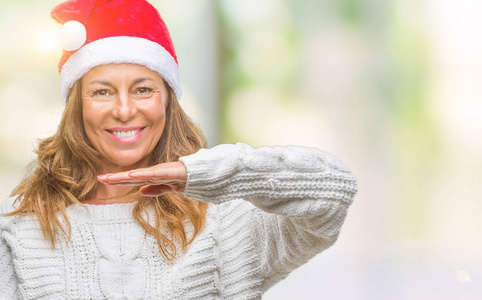 中年老年西班牙裔妇女戴着圣诞帽，在孤立的背景上做手势，双手显示大尺寸的标志符号。 微笑着看着相机。 测量概念。
