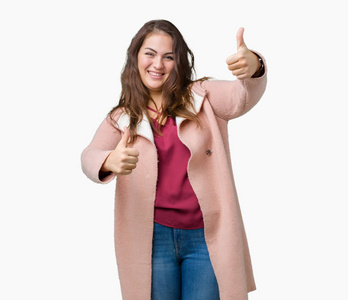 漂亮的加上尺寸的年轻女人穿着冬天的外套，在孤立的背景上，批准用手竖起大拇指做积极的手势，微笑，为成功而高兴。 看着相机赢家的手势