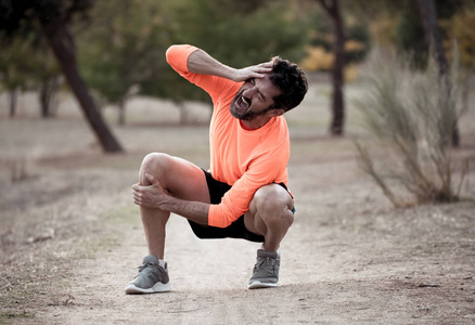 年轻的健身男子抱着膝盖，双手疼痛后，肌肉损伤，骨折，腿部疼痛，扭伤或抽筋，在公园户外跑步锻炼，在运动训练中伤害。
