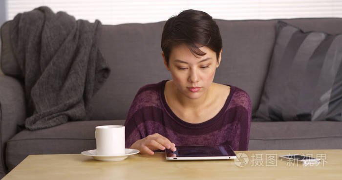 亚洲女人坐在咖啡桌上，端着平板电脑