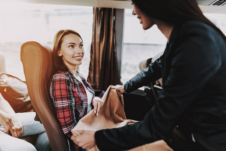 女旅游服务员工在旅游巴士工作。 年轻微笑的女人穿着黑色西装给乘客送毯子。 旅游旅游和人的概念。 旅途中的人。 暑假假期