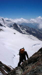 登山者剪影攀登一座陡峭的岩石山峰，高高地耸立在白色和狂野的冰川之上，身后有一片壮丽的景色