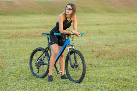 女孩骑着山地车在越野上，美丽的肖像自行车在日落健身女孩骑着现代碳纤维山地自行车。