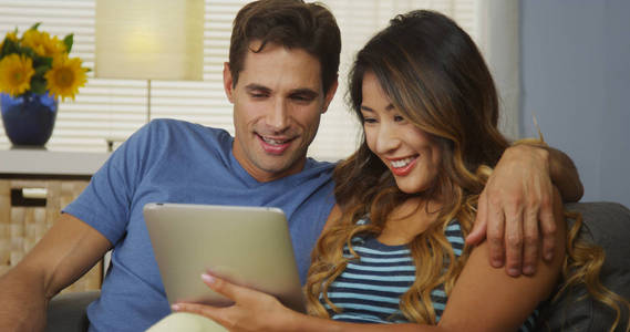 快乐的异族夫妻在沙发上一起使用平板电脑