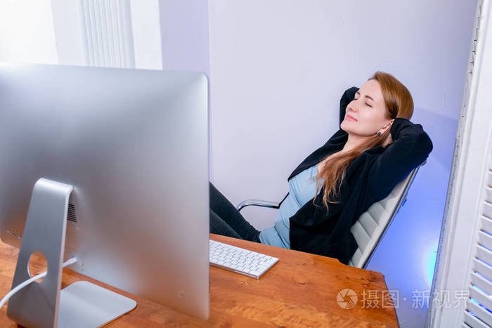 快乐的年轻成功女商人在办公室的肖像. 她坐在桌子旁看着显示器.