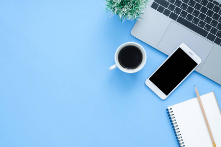 办公桌工作空间平面躺在上面的工作空间模型照片与笔记本电脑智能手机咖啡和笔记本在蓝色的粘贴背景。 彩色蓝底办公桌概念