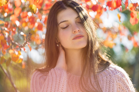 阳光明媚的秋天，美丽的年轻女子穿着时尚的针织毛衣，站在金色的秋天森林里