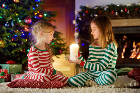快乐的小女孩穿着圣诞睡衣，在舒适的黑暗客厅里玩壁炉