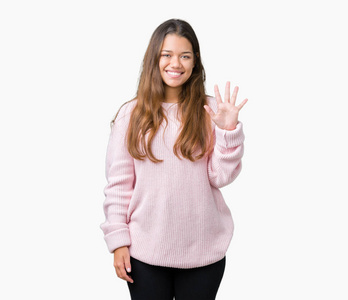 年轻漂亮的黑发女人穿着粉红色的冬季毛衣，在孤立的背景上，用手指举着第五个，微笑着自信和快乐。