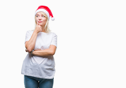年轻漂亮的金发女人戴着圣诞帽，戴着孤立的背景，手托着下巴，思考着问题的沉思表情。 带着体贴的脸微笑。 怀疑概念。