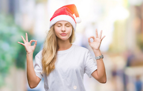 年轻漂亮的金发女人戴着圣诞帽，在孤立的背景上放松，闭着眼睛微笑，用手指做冥想手势。 瑜伽概念。