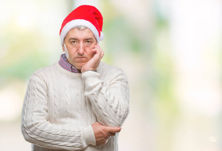 英俊的老人戴着圣诞帽，在孤立的背景下思考，看起来疲惫，厌倦了交叉双臂的抑郁问题。
