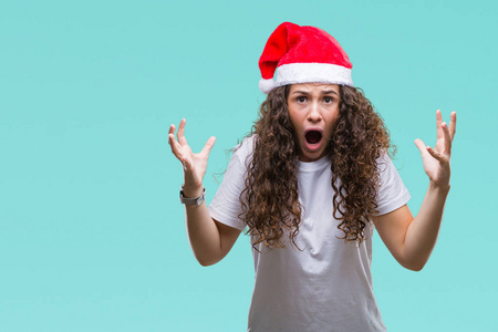 年轻的黑发女孩戴着圣诞帽在孤立的背景上疯狂和疯狂的喊叫和喊叫与侵略性的表情和手臂举起。挫折的概念..