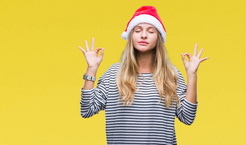年轻漂亮的金发女郎戴着圣诞帽，在与世隔绝的背景下放松，闭着眼睛微笑，用手指做冥想手势。瑜伽概念。