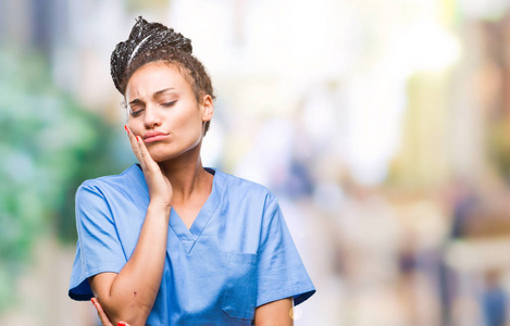 年轻的辫子非裔美国女孩专业护士在孤立的背景下思考，看起来疲惫和无聊的抑郁问题与交叉的手臂。