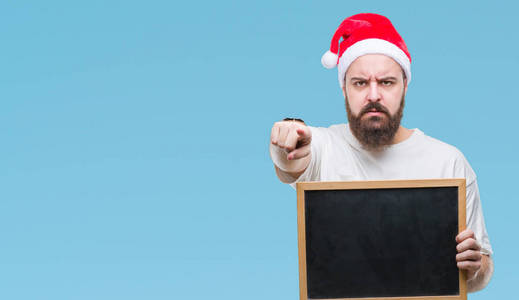 年轻的白种人嬉皮士戴着圣诞帽，手拿黑板，用手指指着相机和你，手势，正面的积极和自信的手势。