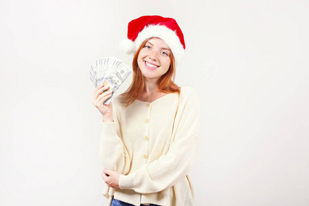 钱作为圣诞礼物的概念。幸福的年轻红头发的女人拿着一堆一百元作为新年礼物收到的肖像。白色被隔绝的背景, 拷贝空间, 关闭