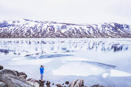 旅游摄影师拍摄挪威春天的雪景照片，人靠近美丽的冰冻湖在山上