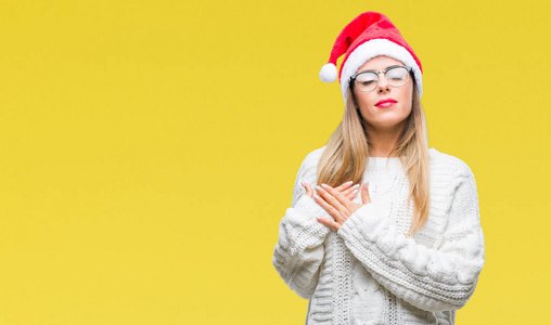 年轻漂亮的女人戴着圣诞帽，在孤立的背景上微笑，双手放在胸前，闭着眼睛，脸上有感激的手势。健康观念。