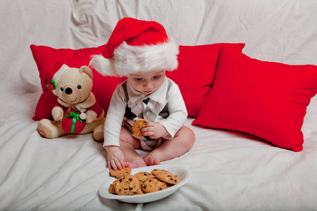 一个戴红帽子的小孩吃饼干和牛奶。一个戴红帽子的婴儿的圣诞摄影。新年假期和圣诞节。