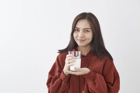 美丽的年轻亚洲女人喝牛奶白色的墙壁背景