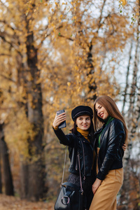 两个微笑的年轻女孩走在秋天公园路上，拍照片