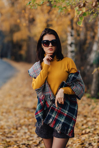 舒适时尚的年轻女孩独自走在秋天的彩色公园里，戴着太阳镜