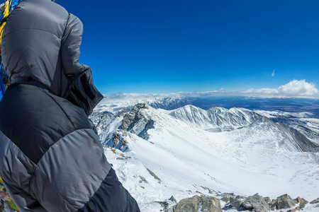 女登山者头盔和羽绒服与徒步杖站在山顶