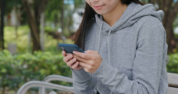 女人用手机坐在城市公园里