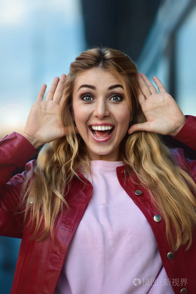 美丽忧郁的金发白人白人女青年的特写肖像,穿着红色夹克在城市街道外