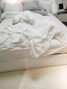 关闭白色床上用品和枕头在墙房的背景, 凌乱的床的概念在晚上
