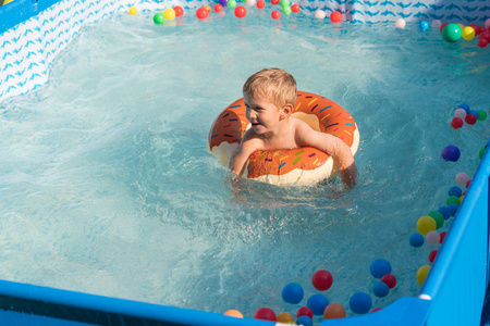 快乐的男孩在炎热的夏天在户外小游泳池里玩五颜六色的充气戒指。 孩子们学会游泳。 儿童水玩具。