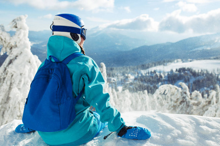 一个冬天穿着蓝色头盔和绿色夹克的漂亮女孩正在山里玩得很开心。 旅游休闲自由运动的概念。 美丽的自然会带来好天气。