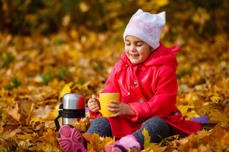 微笑的女孩在秋天公园喝热水瓶里的茶